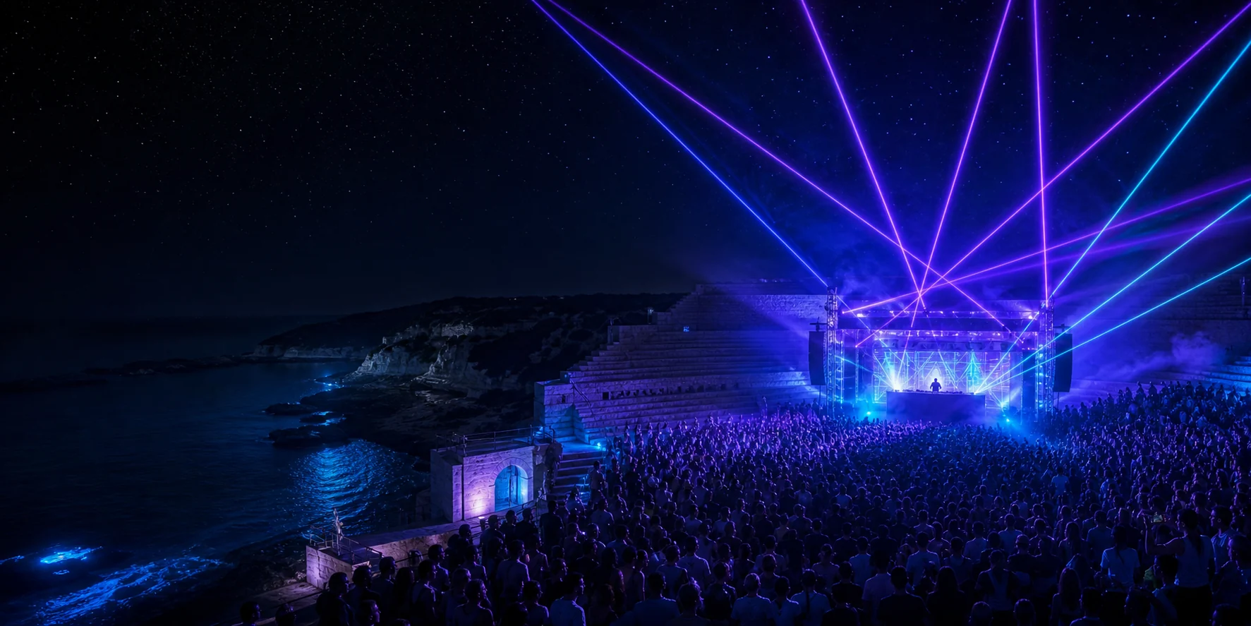 Crowd watching a DJ and laser show in a seaside amphitheatre at night