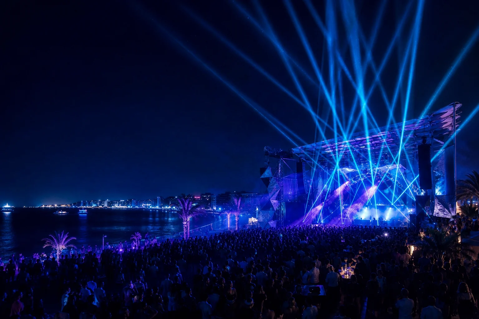 Open-air electronic event with a crowd and blue stage lights by the sea